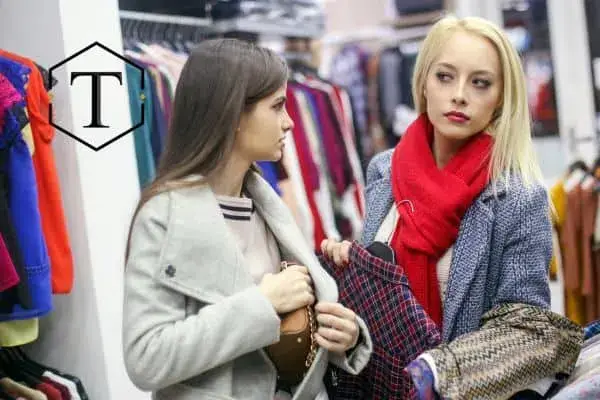 Two women in a store, one of them hiding a piece of clothing.
